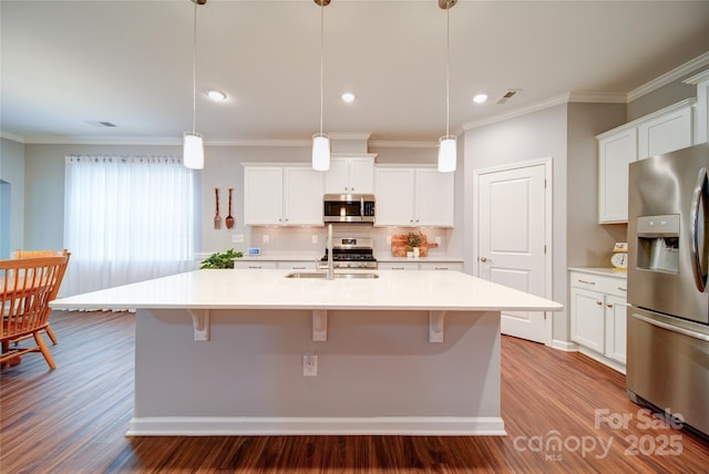 kitchen with appliances with stainless steel finishes, white cabinetry, wood-type flooring, a center island with sink, and decorative light fixtures