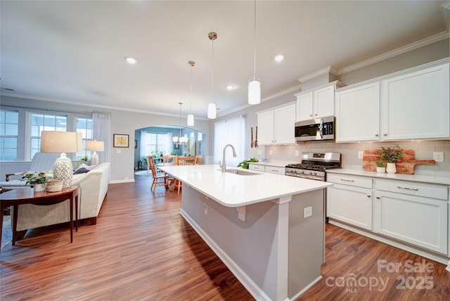 kitchen with pendant lighting, sink, appliances with stainless steel finishes, white cabinetry, and an island with sink