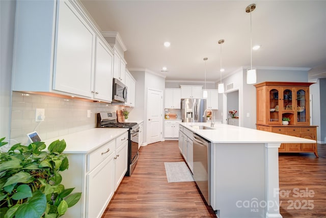 kitchen with decorative light fixtures, a center island with sink, white cabinets, stainless steel appliances, and backsplash