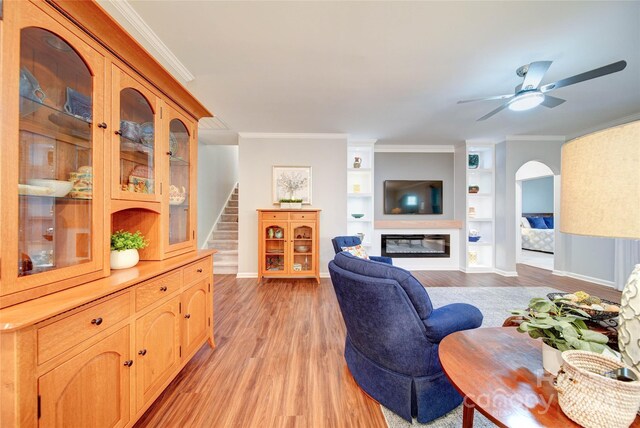 living room with built in shelves, ornamental molding, light hardwood / wood-style floors, and ceiling fan