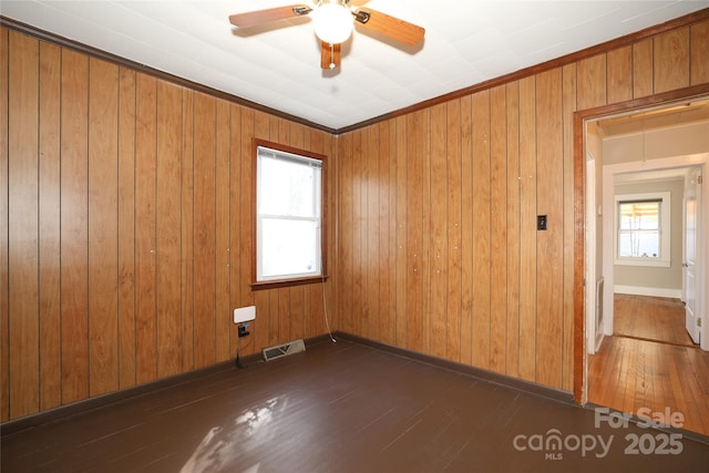 spare room with crown molding, dark hardwood / wood-style floors, wooden walls, and ceiling fan