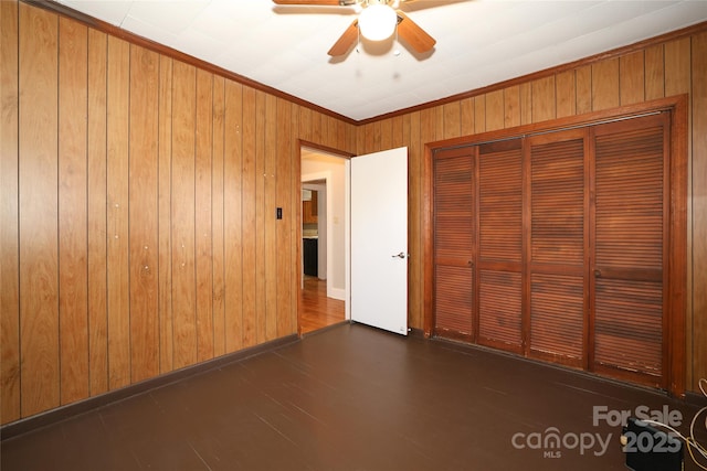 unfurnished bedroom featuring dark wood-type flooring, ceiling fan, ornamental molding, a closet, and wood walls