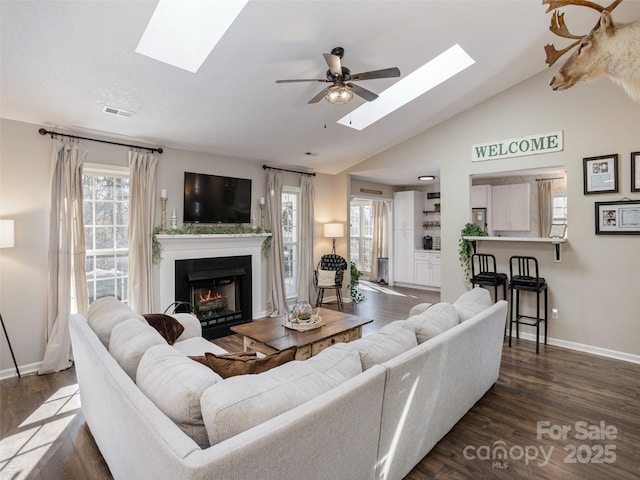 living room featuring dark wood-type flooring, ceiling fan, and vaulted ceiling with skylight