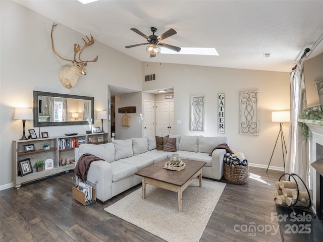 living room with ceiling fan, lofted ceiling with skylight, dark hardwood / wood-style floors, and a textured ceiling