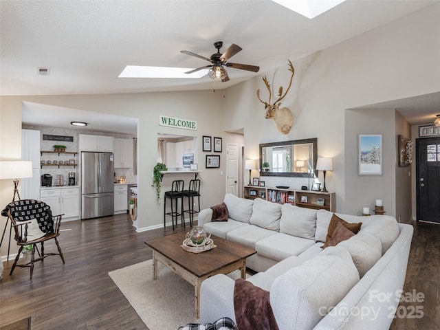 living room with ceiling fan, vaulted ceiling with skylight, dark wood finished floors, and visible vents