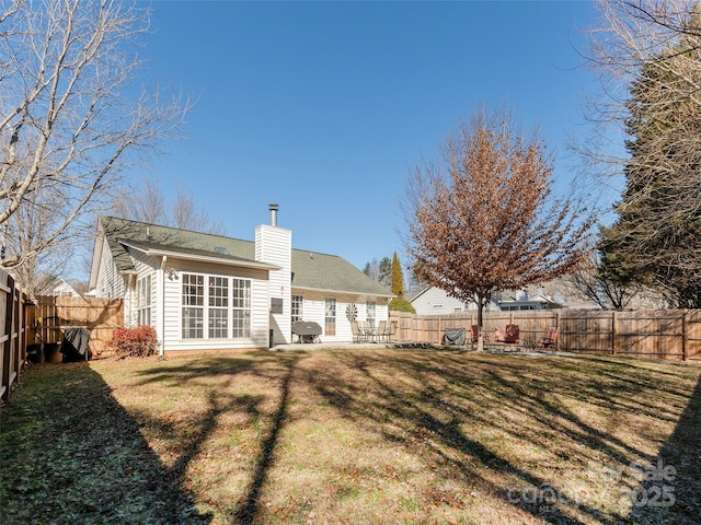 back of house with a fenced backyard, a yard, and a chimney