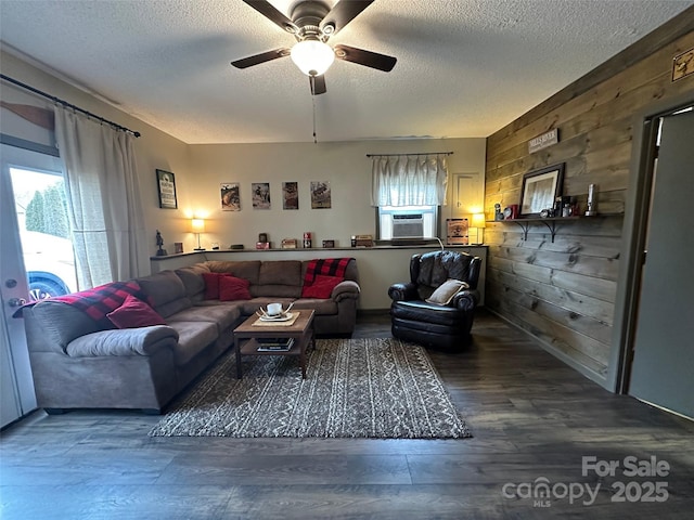 living room featuring wood walls, ceiling fan, a textured ceiling, and wood finished floors