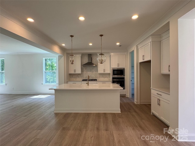 kitchen with built in microwave, stainless steel oven, backsplash, wood finished floors, and wall chimney range hood