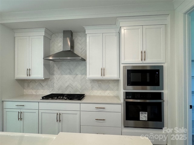 kitchen with wall chimney exhaust hood, stainless steel appliances, white cabinetry, and tasteful backsplash
