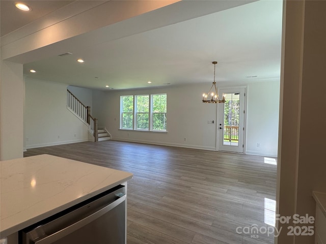 unfurnished living room featuring plenty of natural light, a notable chandelier, wood finished floors, and stairway