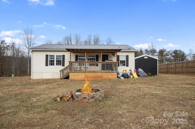 rear view of property with a lawn, a deck, a shed, and an outdoor fire pit