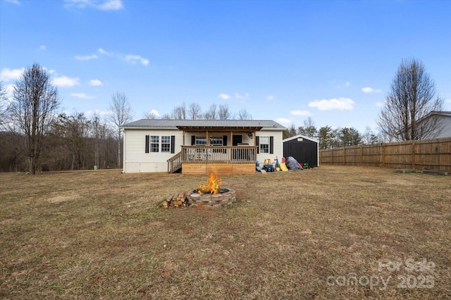 back of property with a shed, a wooden deck, a yard, and an outdoor fire pit