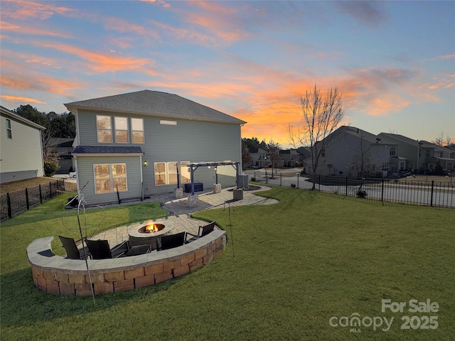 back house at dusk with an outdoor fire pit, a patio, and a lawn