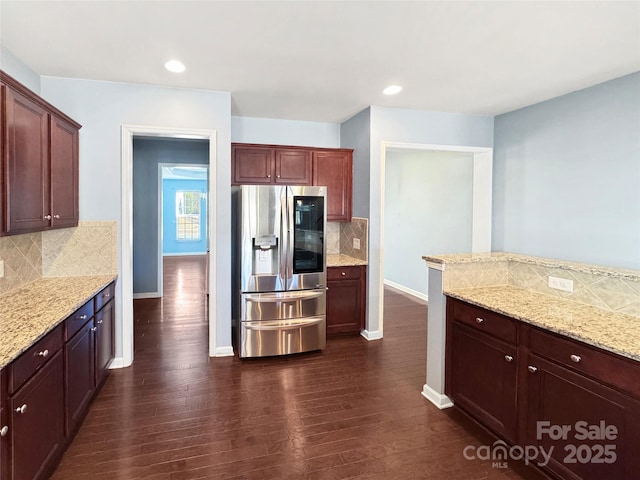 kitchen with tasteful backsplash, light stone counters, dark hardwood / wood-style flooring, and stainless steel refrigerator