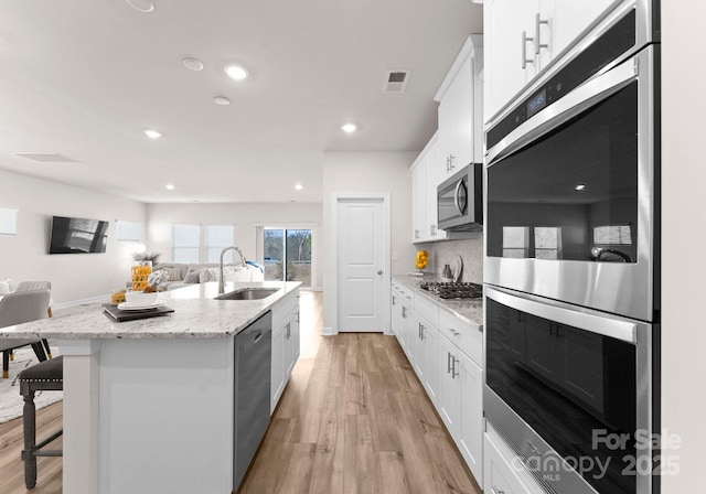 kitchen with white cabinetry, sink, a breakfast bar area, stainless steel appliances, and a center island with sink