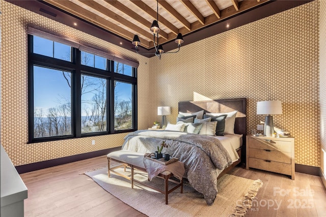 bedroom with wallpapered walls, wood-type flooring, baseboards, and beam ceiling