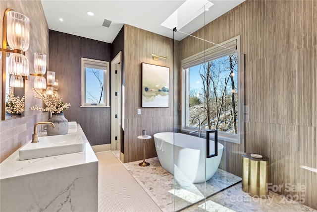 bathroom featuring vanity, a bath, a skylight, and tile walls