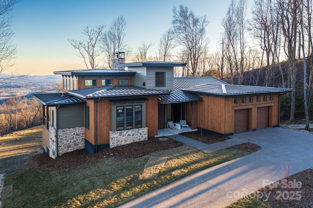 view of front of property featuring metal roof, stone siding, concrete driveway, a standing seam roof, and a chimney