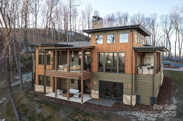 rear view of house with a patio, stone siding, a sunroom, metal roof, and a standing seam roof