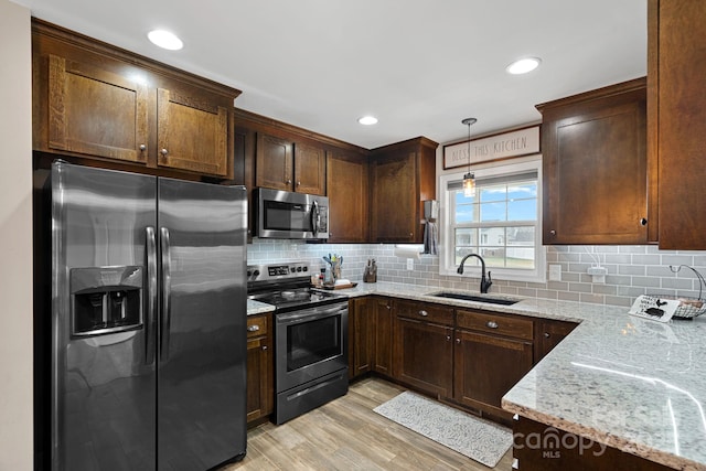 kitchen featuring sink, appliances with stainless steel finishes, hanging light fixtures, light hardwood / wood-style floors, and light stone countertops