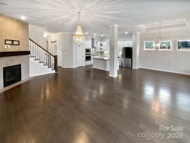 unfurnished living room with an inviting chandelier, a fireplace, a raised ceiling, and dark wood-type flooring