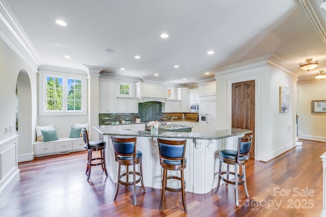 kitchen featuring stone countertops, wood-type flooring, a breakfast bar area, white cabinets, and a large island with sink