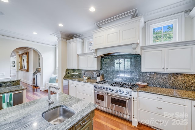 kitchen with tasteful backsplash, white cabinetry, sink, dark stone counters, and double oven range