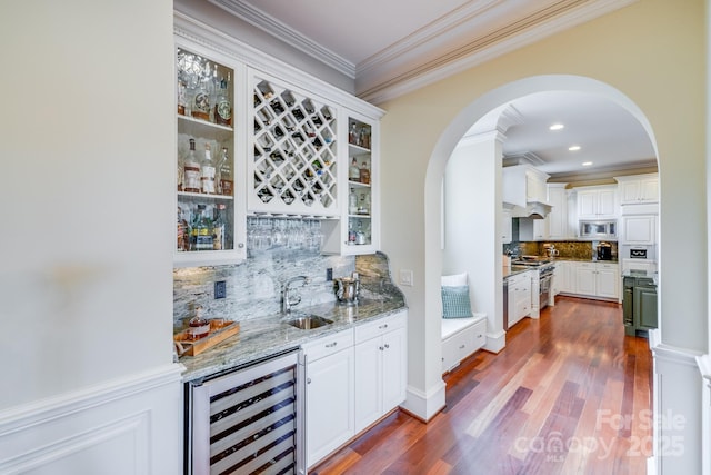 bar with appliances with stainless steel finishes, white cabinetry, sink, beverage cooler, and light stone counters