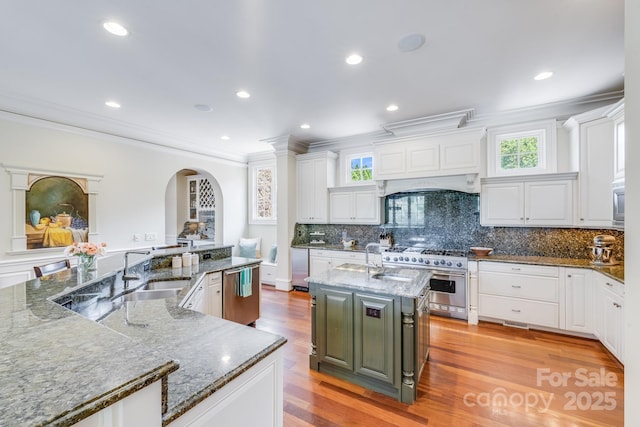 kitchen featuring stone counters, sink, stainless steel appliances, a center island with sink, and light wood-type flooring