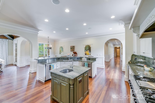 kitchen featuring sink, appliances with stainless steel finishes, a kitchen island with sink, hanging light fixtures, and dark stone countertops