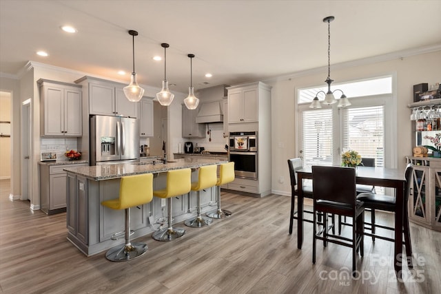 kitchen with a breakfast bar, gray cabinetry, stainless steel appliances, light stone countertops, and a center island with sink