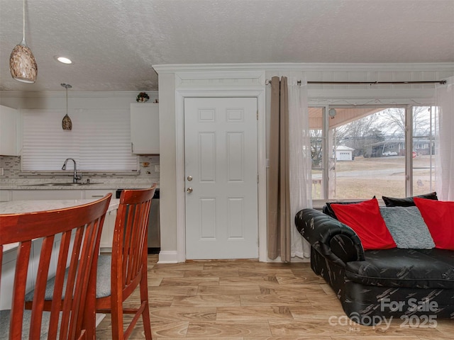 kitchen featuring decorative light fixtures, sink, white cabinets, crown molding, and a textured ceiling