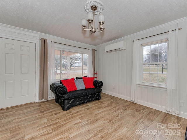 sitting room with an inviting chandelier, a wall mounted AC, a textured ceiling, and light hardwood / wood-style floors