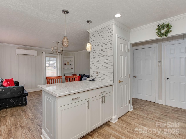 kitchen with an AC wall unit, pendant lighting, white cabinets, ornamental molding, and a textured ceiling