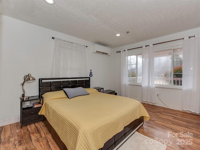 bedroom featuring a wall mounted air conditioner, hardwood / wood-style floors, and a textured ceiling