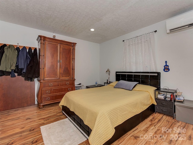 bedroom featuring a wall mounted AC, a textured ceiling, and light hardwood / wood-style flooring