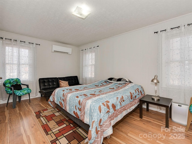 bedroom with multiple windows, hardwood / wood-style floors, a textured ceiling, and a wall unit AC