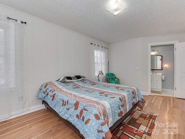 bedroom featuring crown molding, ensuite bath, a textured ceiling, and hardwood / wood-style flooring