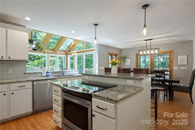 kitchen featuring appliances with stainless steel finishes, decorative light fixtures, white cabinetry, sink, and a breakfast bar area