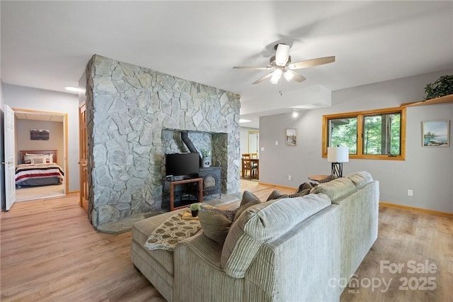 living room featuring a wood stove, ceiling fan, and light hardwood / wood-style flooring