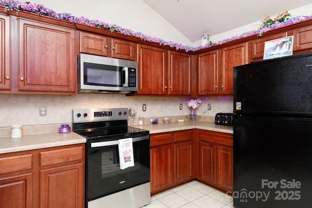 kitchen with appliances with stainless steel finishes, light tile patterned floors, lofted ceiling, and backsplash