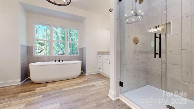 full bath with a freestanding bath, a chandelier, wood finished floors, and a shower stall