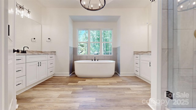 full bath with an inviting chandelier, wood finished floors, a soaking tub, baseboards, and vanity