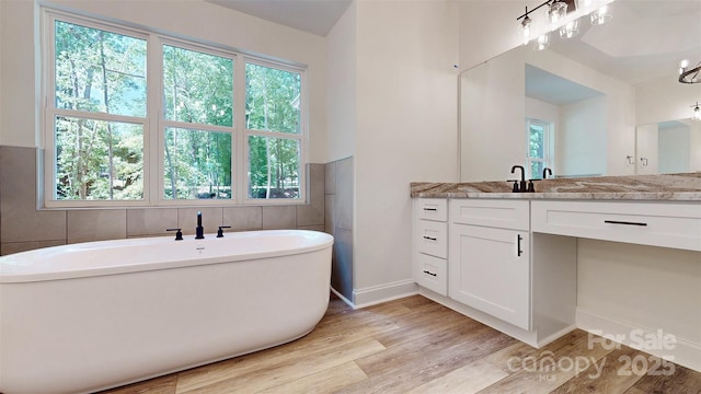 full bath featuring baseboards, vanity, a freestanding tub, and wood finished floors