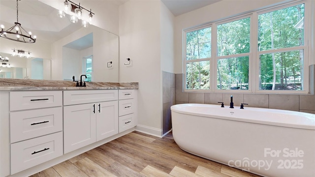 full bathroom featuring wood finished floors, a soaking tub, baseboards, a chandelier, and vanity