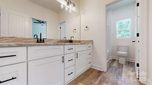full bathroom with a sink, toilet, wood finished floors, double vanity, and baseboards