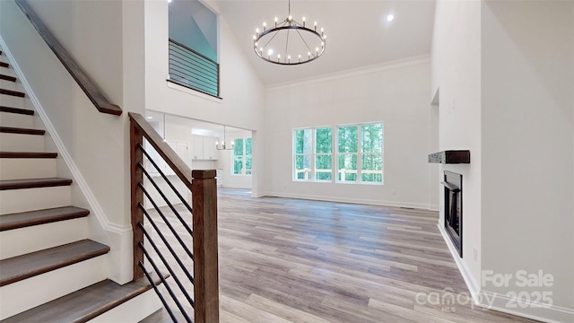 unfurnished living room with stairway, a chandelier, a high ceiling, and light wood-style floors