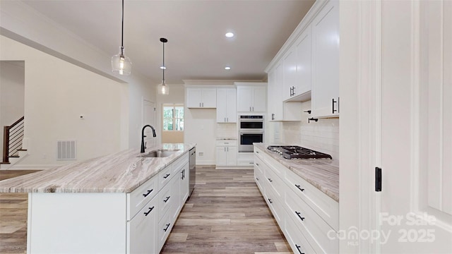 kitchen with visible vents, a sink, decorative backsplash, light wood-style floors, and appliances with stainless steel finishes