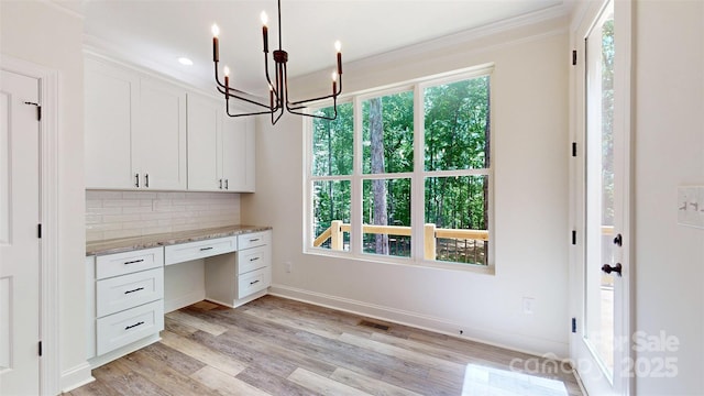 unfurnished office with light wood-style flooring, ornamental molding, an inviting chandelier, visible vents, and built in study area