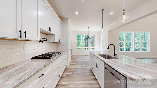 kitchen featuring light wood-style flooring, a sink, white cabinetry, backsplash, and stainless steel appliances